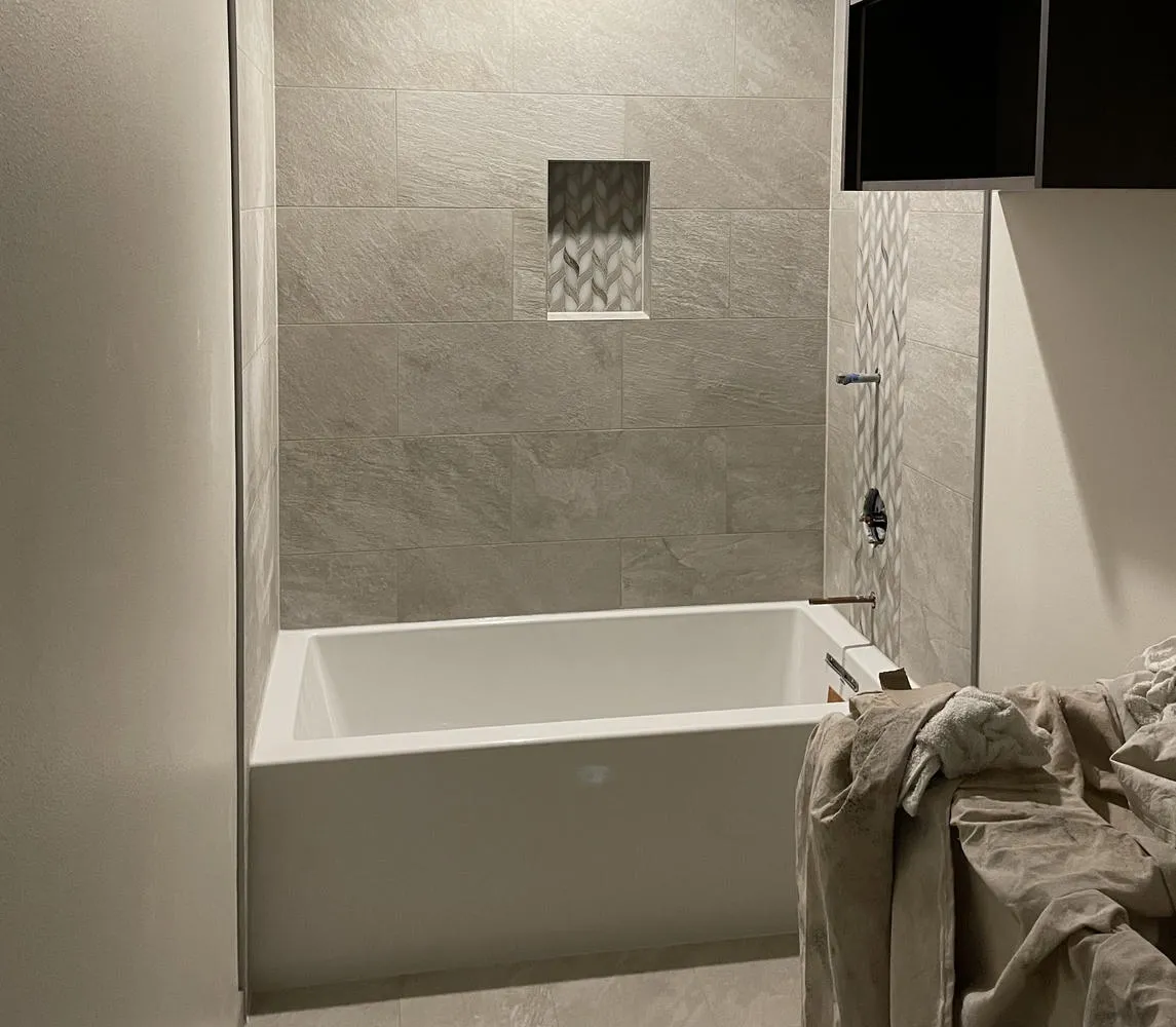 A white bathtub in a tiled shower area with a niche, and a dark brown cabinet above a counter.